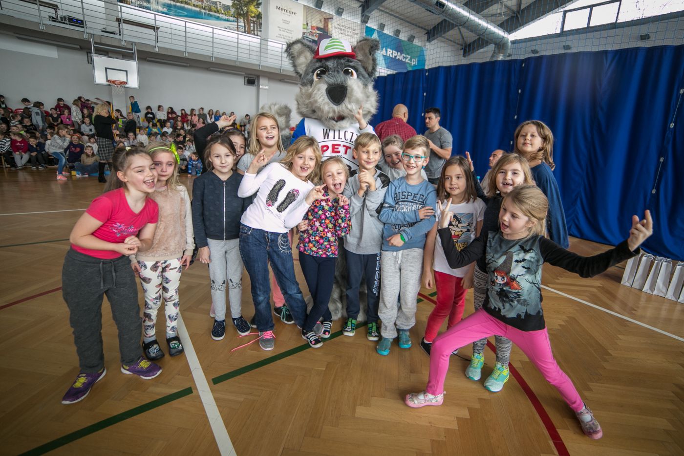 Na fotografii widnieje wilk przebranie pozujący do fotografii z grupą młodzieży